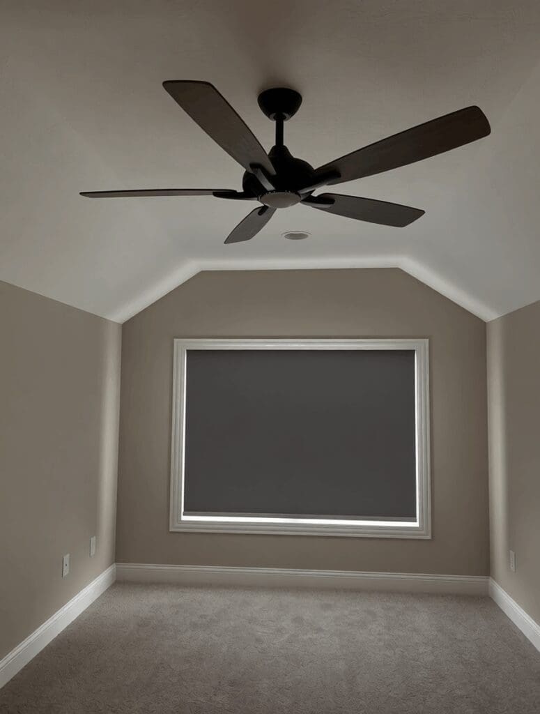 An empty room with a ceiling fan has blackout shades on the window.