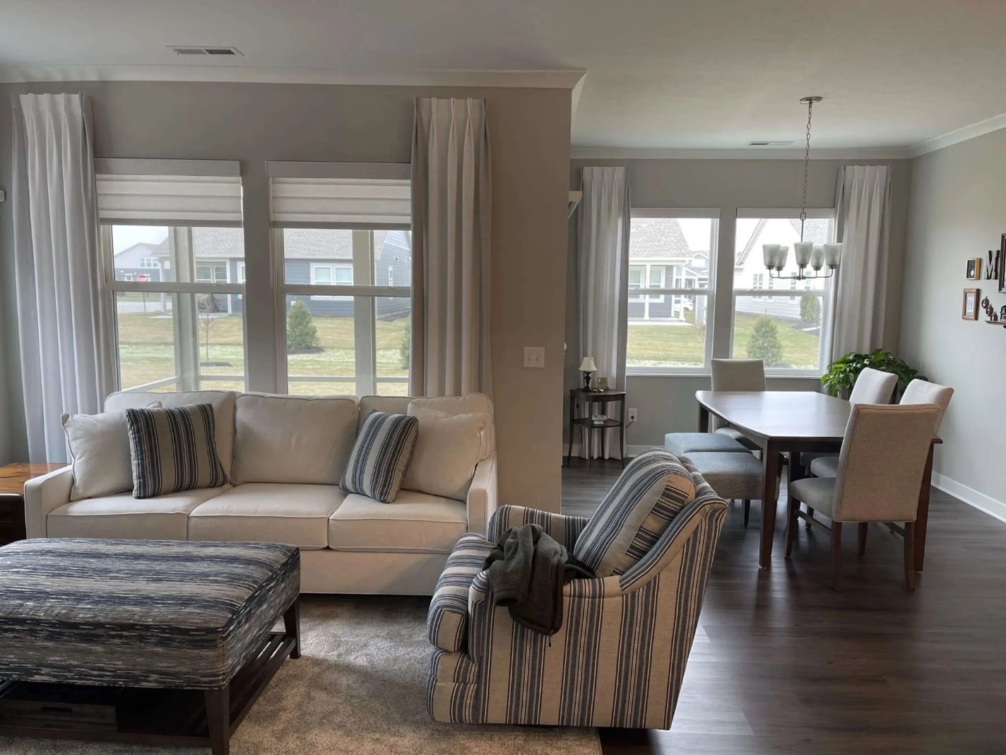 A living room in grey neutrals has full length drapes on the large windows.